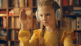 Diligent schoolgirl in headset raising hand during online video lesson on laptop