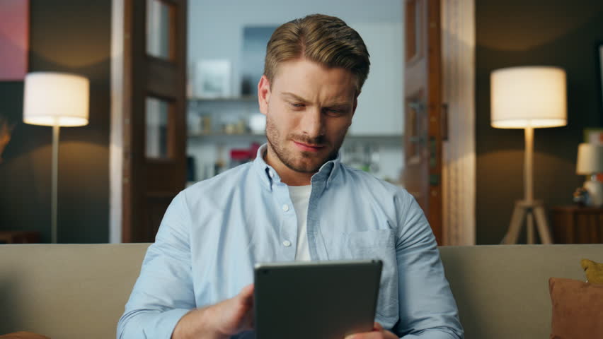 Surprised guy looking tablet screen at evening zoom on. Wondering guy watching tab computer trying understand at home closeup. Confused focused man holding digital pad device finding mistake at work Royalty-Free Stock Footage #1102856293