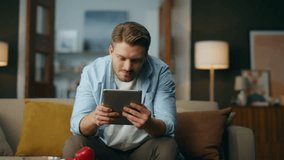 Positive man using tab computer at home. Optimistic guy working pad sitting sofa in living room. Relaxed businessman holding digital tablet browsing online. Smiling freelancer examining file remotely  - Powered by Shutterstock - Get 15% off with code: PIKWIZARD15