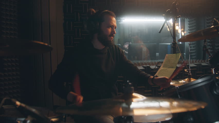 Male musician in headphones plays a drum set. Drummer records song in soundproof music recording room. Audio engineer on background. Work in the sound recording studio. Concept of music production. Royalty-Free Stock Footage #1102856917