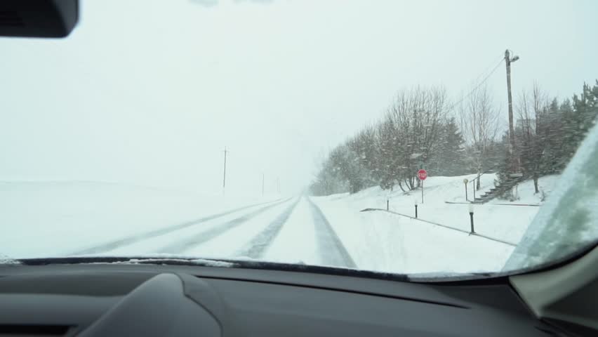 View from the windshield of a car that is driving along a snowy rural road in a snowstorm, snowflakes fly into the windshield, slow motion Royalty-Free Stock Footage #1102861179