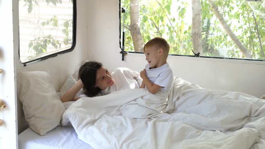 Young mother wakes up in the morning next to her son during a summer trip in a mobile home. Royalty-Free Stock Footage #1102862295