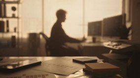 Blurred silhouette of a young man typing on a computer keyboard and drinking coffee in a dark office in the evening. Manager works sitting at a table near a window with backlight. - Powered by Shutterstock - Get 15% off with code: PIKWIZARD15