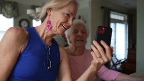 Happy smiling, laughing mature blonde woman holds phone with elderly senior mother having video chat on phone. Smiling blonde lady talking to family on smartphone.