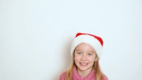 A little blond girl in red Santa Claus hat is actively telling something and looking at the camera. The girl sings or recites a poem. Video portrait. 4k resolution video.
