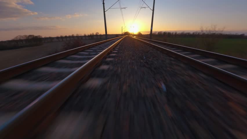 Railway railroad aerial drone shot, FPV shot with hyperlapse like movement, flying towards a sunset horizon with fast speed on the tracks.