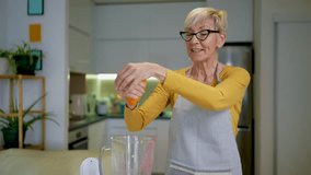 Senior woman in casual home clothes prepares healthy cocktails with different seasonal fruits.