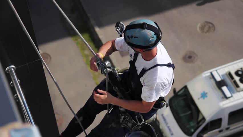 High Angle View of Window Washer Hanging on Climbing Ropes and Washing the Windows and Facade of a Modern High-Rise Building. Commercial Window  Cleaning. Occupational Hazards in Window Cleaning.