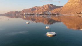 Aerial video over a small salt island of the Dead Sea, low flight in the background of the hotels at sunrise