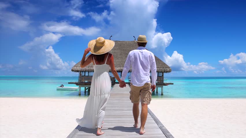 A happy holiday couple in white summer clothing walks down a wooden pier  in the Maldives islands, Indian Ocean Royalty-Free Stock Footage #1102875441