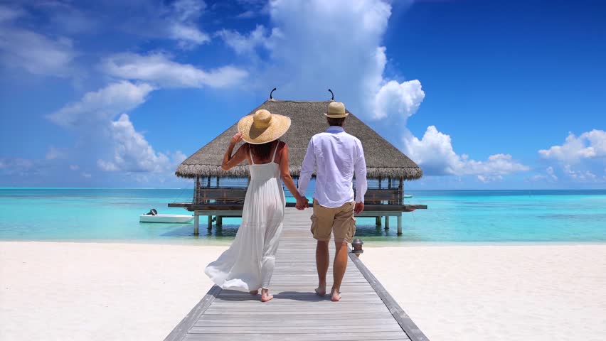 A happy holiday couple in white summer clothing walks down a wooden pier  in the Maldives islands, Indian Ocean | Shutterstock HD Video #1102875441
