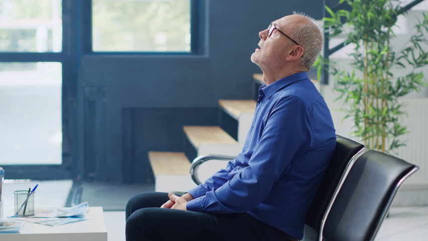 Stressed senior man waiting in hospital lobby to meet with general practitioner, sitting on chiar in reception before consultation. Elderly patient having medical appointment. Medicine service