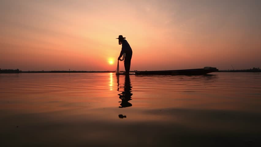 Silhouette fisherman throwing net casting fish in early morning with wooden boat fisherman life style. Royalty-Free Stock Footage #1102876577