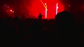 People at a musical rock concert. A person records the band's performance on a smartphone. Club atmosphere, flashing multicolored rays of light. Rear view. The concept of entertainment.
