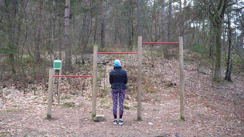 Static shot of women doing pull-ups on a bar in the forest for exercise