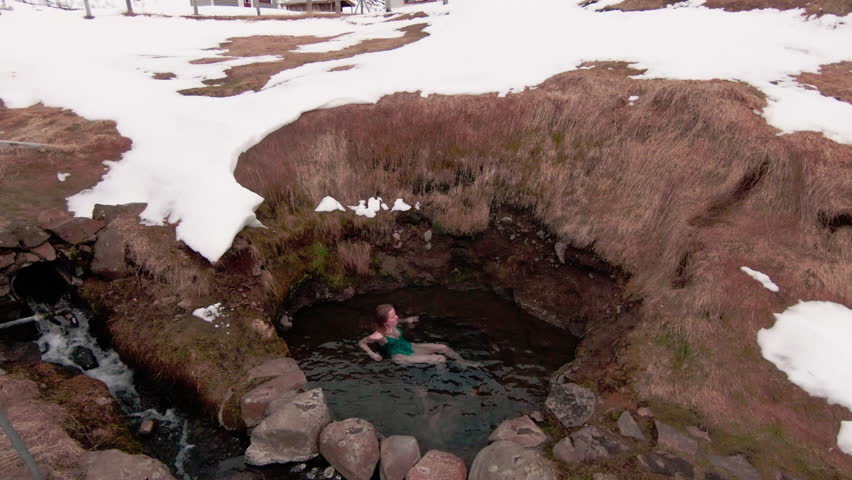 Ascend view, caucasian woman bathing in remote natural hot spring, next to pool. Iceland