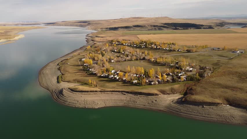 Aerial campground in autumn colours along a lake with low water levels overlooking distant windmills spinning at the Old Man Dam Alberta.