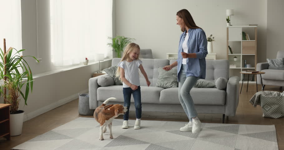 Energetic young cheerful mother dance in cozy living room together with little daughter and dog, listen moving to music, looks carefree, enjoy pastime at home, family celebrate vacation feel happy Royalty-Free Stock Footage #1102892495