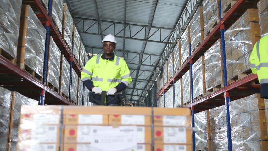 Worker in auto parts warehouse use a handcart to work to bring the box of auto parts into the storage shelf of the warehouse waiting for delivery to the car assembly line