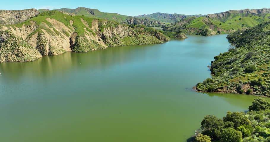 Aerial pullout reveal fly over a California lake and reservoir full of water with green hills and mountains landscape on a sunny day. Lake Piru