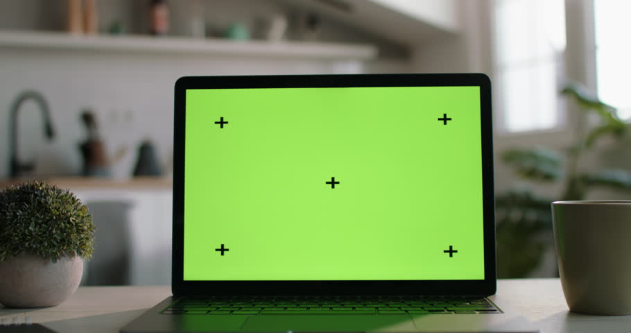 Laptop with green screen on display on kitchen table. Mockup of laptop with chromakey screen. Laptop on table is configured for work, business and study, mockup template for inserting videos or photos Royalty-Free Stock Footage #1102895851