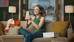 Emotional girl rejoicing mobile phone at home. Shopping addicted person sitting sofa ordering new items. Happy smiling woman dancing hands with smartphone relaxing around boxes and clothes alone - Powered by Shutterstock - Get 15% off with code: PIKWIZARD15