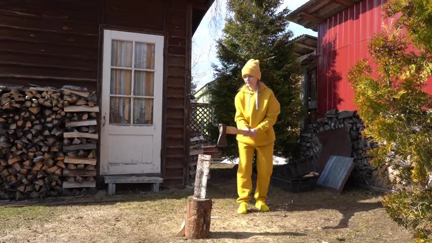 A woman in a yellow suit is chopping wood with an axe.