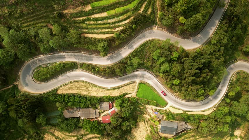 Windy road with traffic weaving through lush layered hillside rice paddy plantations in North Vietnam countryside. Drone bird
