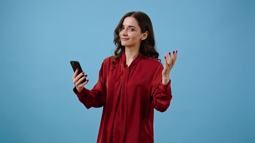 Successful woman works on phone app and recommends useful program showing thumb-up. Lady calls for participation pointing finger at device against blue wall