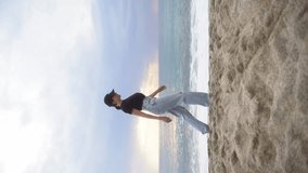  A young woman in light jeans walks straight down the beach. Vertical video