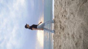  A young woman in light jeans walks straight down the beach. Vertical blurred video
