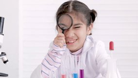 Scientist elementary girl wearing gown suit using magnifying glass in chemistry classroom, Young science kid studying an experiment in laboratory, Dreams career for childhood education concept, - Powered by Shutterstock - Get 15% off with code: PIKWIZARD15