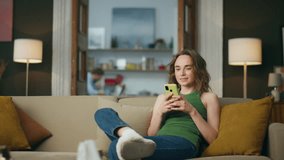 Smiling girl chatting cellphone at home. Positive lady holding mobile phone browsing social media at domestic atmosphere. Relaxed woman reading message sitting sofa. Girl looking at smartphone screen  - Powered by Shutterstock - Get 15% off with code: PIKWIZARD15