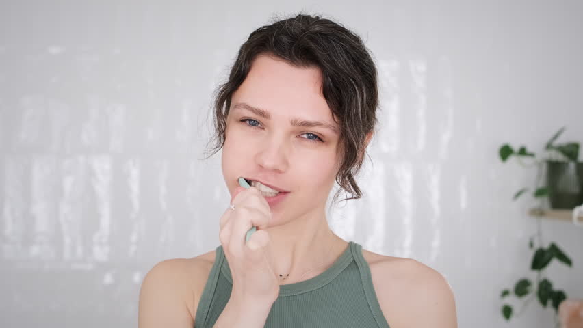 Deep cleaning of teeth. Mirror pov portrait of cute young woman brushing her teeth with recycled plastic toothbrush, caring about her dental hygiene at home. Morning dental care routine in bathroom Royalty-Free Stock Footage #1102920221