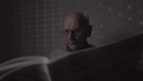 Thoughtful old man with high temples in glasses attentively reads newspaper. Elderly male turns page of newspaper while sitting in evening room - Powered by Shutterstock - Get 15% off with code: PIKWIZARD15