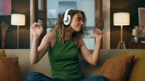 Excited woman dancing indoors sitting sofa. Happy woman enjoying music moving hands at domestic interior zoom on. Carefree girl throwing head back delighting favourite song at home weekend closeup - Powered by Shutterstock - Get 15% off with code: PIKWIZARD15