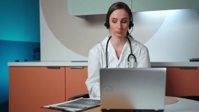 A competent female doctor in a lab coat explains X-ray scanning during a video call with a patient on a laptop