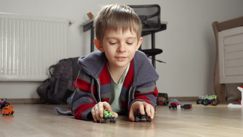Happy smiling boy making a toy car race on wooden floor in bedroom. Children playing alone, development and education, games at home