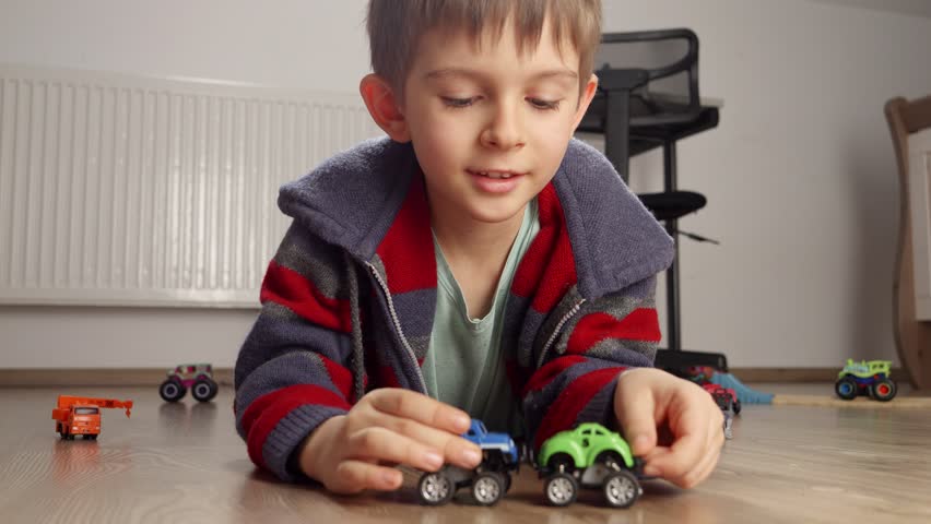 Portrait of cute boy lying on floor and playing with two toy cars. Children playing alone, development and education, games at home