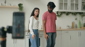 Two active bloggers record funny video clip in kitchen multiracial arabian woman indian man couple dancers dancing to trend music. Mobile phone camera on tripod recording dance motion synchronous move