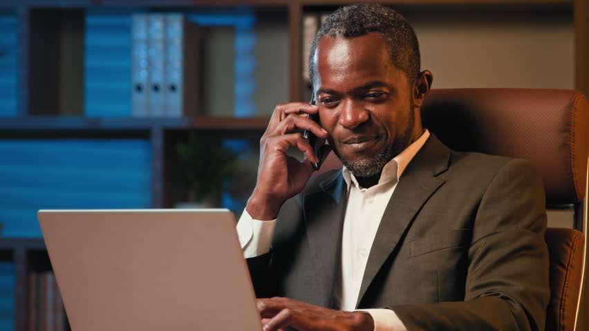Professional manager businessman speak on phone african american man work on laptop make mobile call consult client use smartphone confirm order in online store salesman talking remote with customer Royalty-Free Stock Footage #1102934945