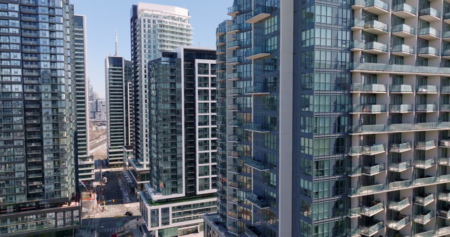 Backward retreat of Drone footage in Liberty Village, Toronto, with modern condos in the immediate foreground and CN Tower visible in distance. Glimpse of  lake and Gardiner Expressway in the shot.