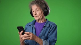 Funny crazy slow motion of happy toothless old elderly grandmother dancing with headphones on with smart phone in hand isolated on green screen background.