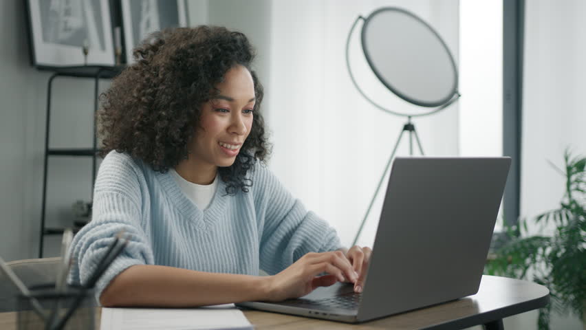 Portrait of beautiful authentic African American female in stylish living room using laptop computer at home. Woman of color browsing Internet and checking videos on Social Networks. Having Fun online | Shutterstock HD Video #1102940133