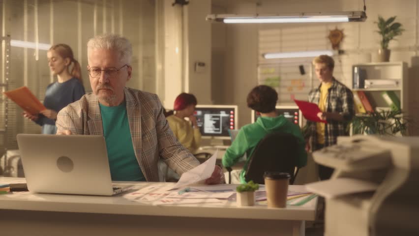 Aged man looks at information on a laptop screen and in a paper chart and is very upset. Angry businessman angrily crumples a sheet of paper and throws it away. Royalty-Free Stock Footage #1102941757