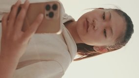 VERTICAL VIDEO, girl in sportswear uses the phone while standing on the waterfront at morning time