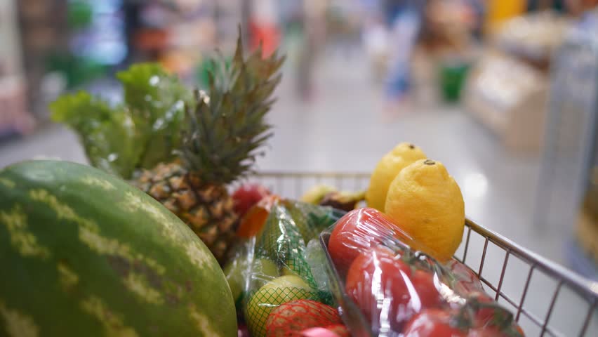 Close-up of fruits and various products in a shopping cart at a grocery store or supermarket.