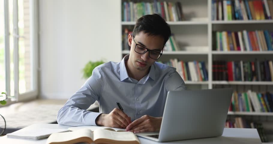 Indian teen student guy in glasses studying in university library, engrossed in creative task making, prepare for admission, doing coursework using laptop. Education, modern technology, intelligence Royalty-Free Stock Footage #1102943943