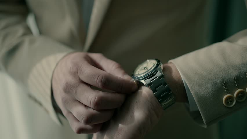A businessman in a suit adjusts a wristwatch.