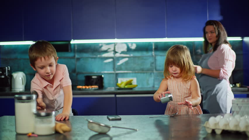 Caucasian children have fun and dance in the kitchen while helping their mother cook. Smiling boy and girl sing and fool around together. Lifestyle of a happy family life. High quality 4k footage Royalty-Free Stock Footage #1102944733